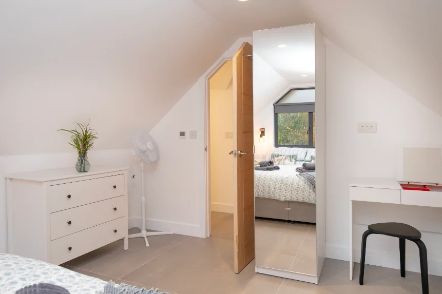 Mirrored wardrobe, small white dressing table and white chest of drawers in a bedroom under sloping eaves
