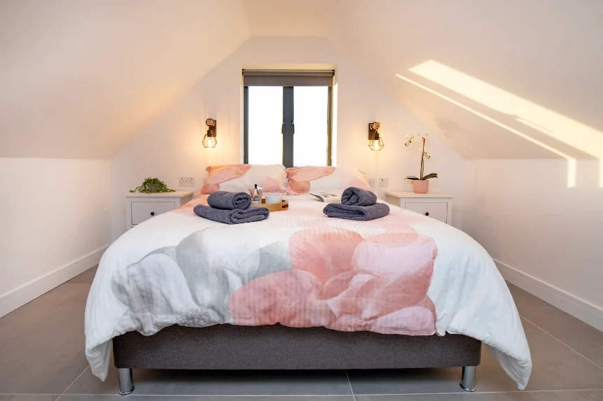 Double bed with white and pink duvet and fresh dark grey towels in a modern bedroom under sloping eaves.
