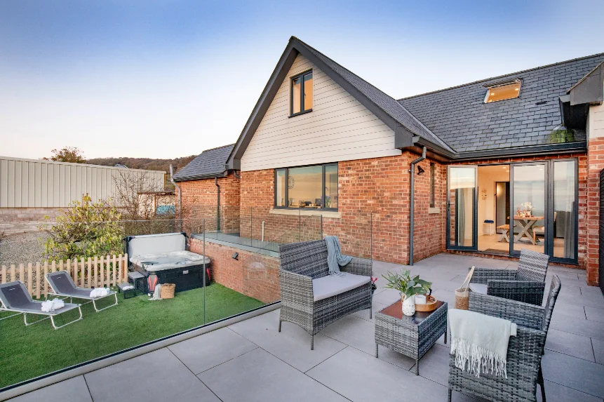 Exterior of Deer View Devon a modern red brick house with hot tub and grey garden furniture on paved patio.