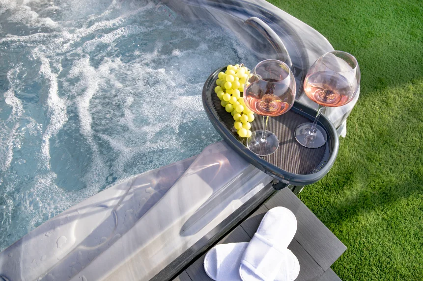 Grey hot tub with tray with two glasses of rose wine and a bunch of grapes balanced on the edge.