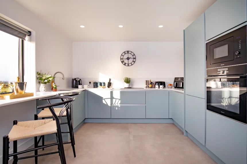 Modern fitted kitchen with blue grey kitchen units incorporating an eye level oven and breakfast bar at the window