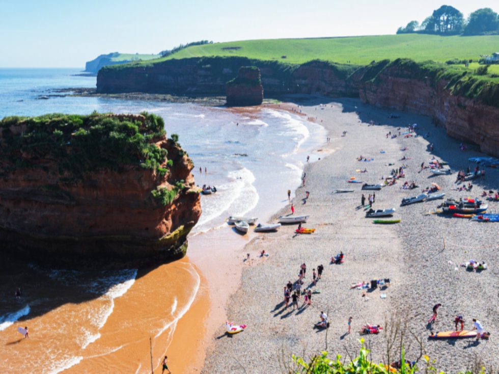 Tourists with small boats and canoes on the beach at Ladram Bay in Devon