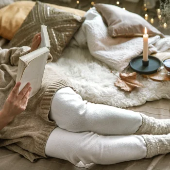 A woman in beige and white casual clothes lying down reading a book